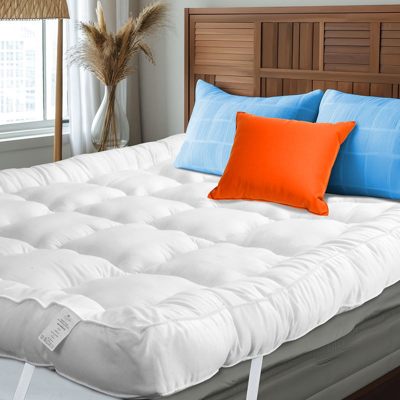 White mattress topper on a bed with blue and orange pillows, wooden headboard, and window in the background