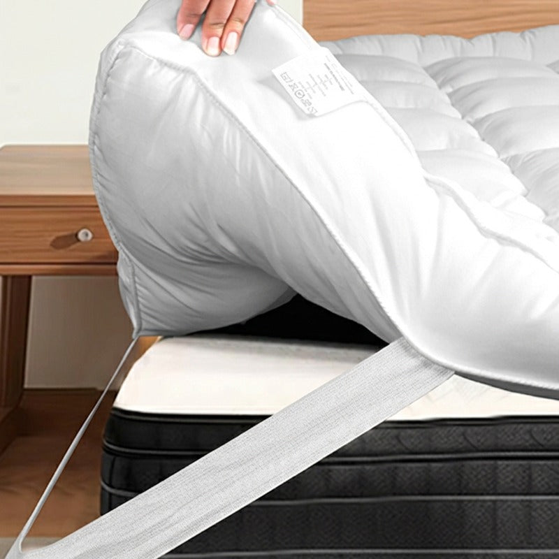Person lifting a mattress topper over mattress by stretching its elastic strip